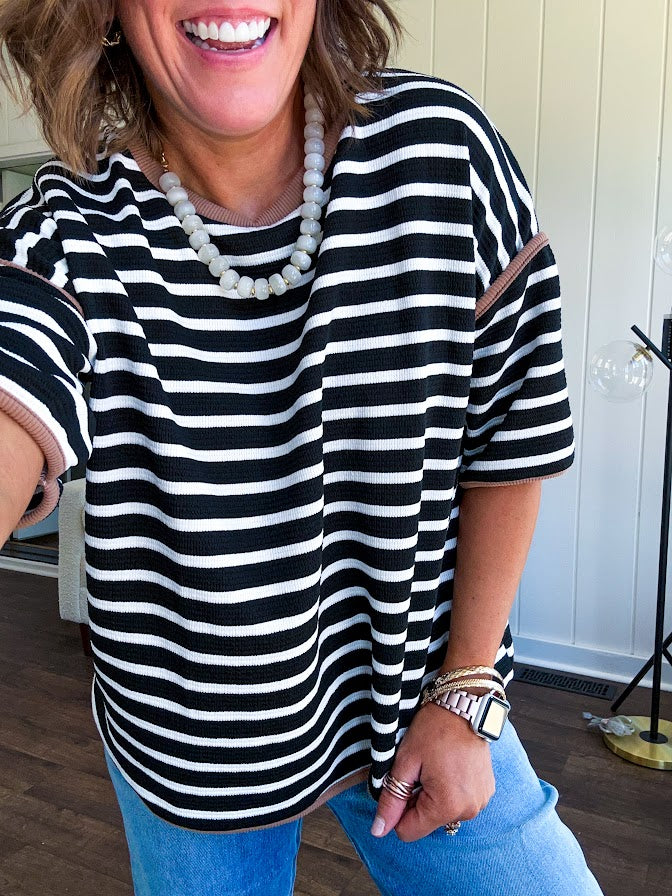 Soft, lightweight stretchy fabric in stripes including black and white, cream and white with contrasting trim at the round neck, hemline and sleeves. short sleeved and boxy cut.