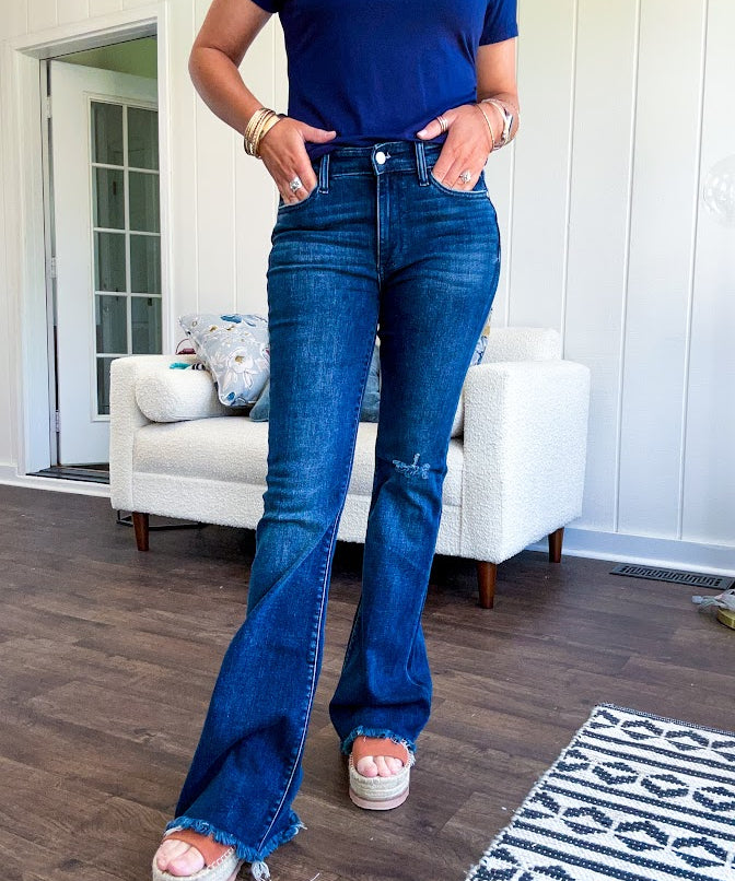 Dark wash flare denim with destroyed hem and minimal distressing on one knee with stretch and mid rise.