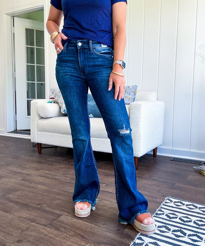 Dark wash flare denim with destroyed hem and minimal distressing on one knee with stretch and mid rise.