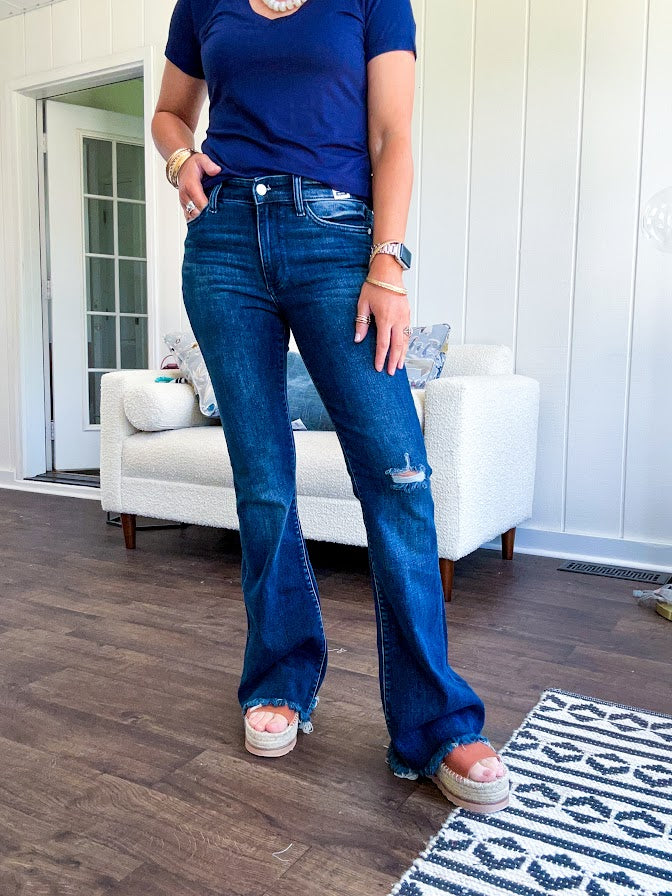 Dark wash flare denim with destroyed hem and minimal distressing on one knee with stretch and mid rise.