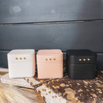 Square leather jewelry travel box with magnetic closure, individual transparent plastic zip closure bags inside and three gold balls on the front. Available in white, pink or black.