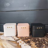 Square leather jewelry travel box with magnetic closure, individual transparent plastic zip closure bags inside and three gold balls on the front. Available in white, pink or black.