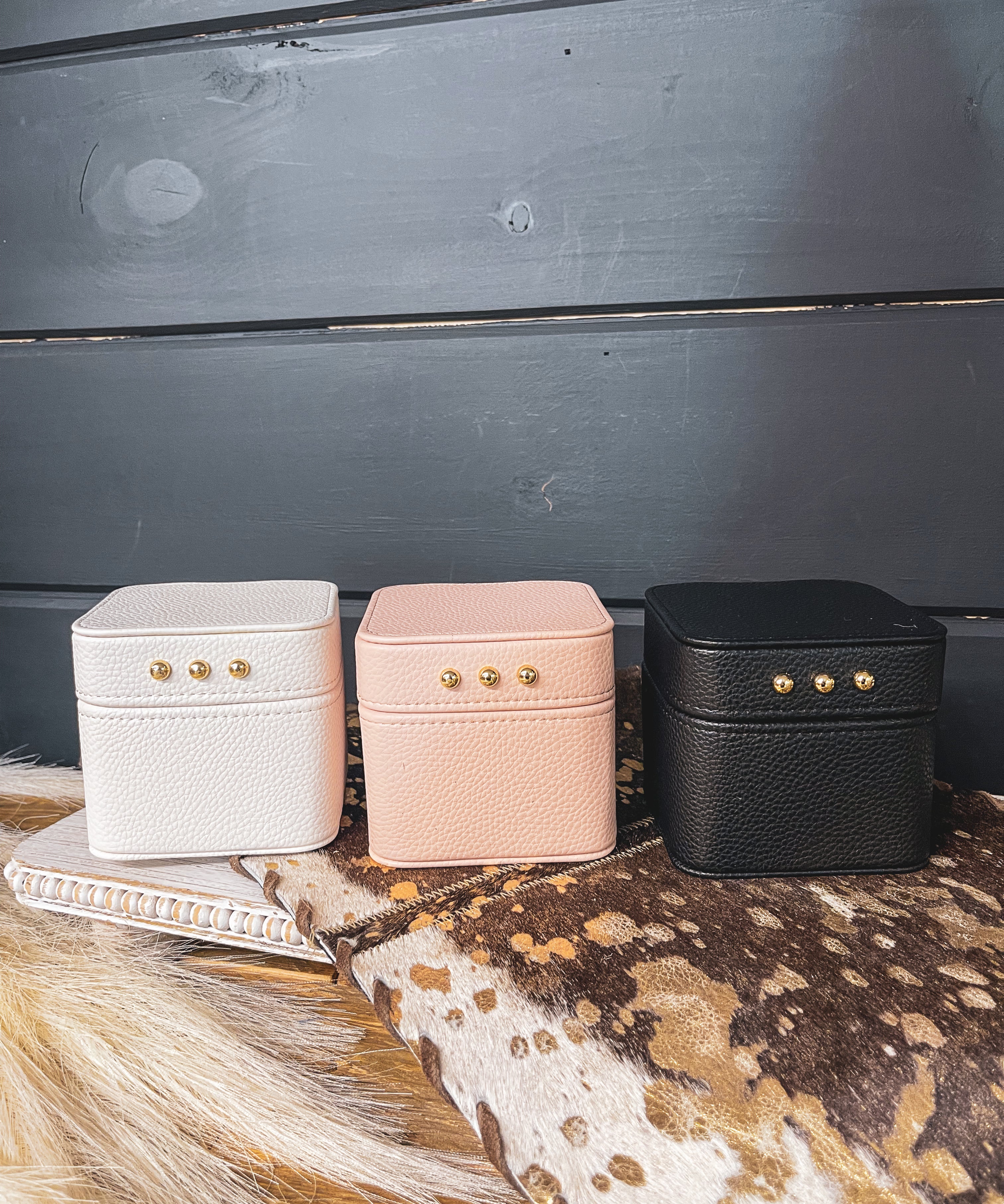 Square leather jewelry travel box with magnetic closure, individual transparent plastic zip closure bags inside and three gold balls on the front. Available in white, pink or black.