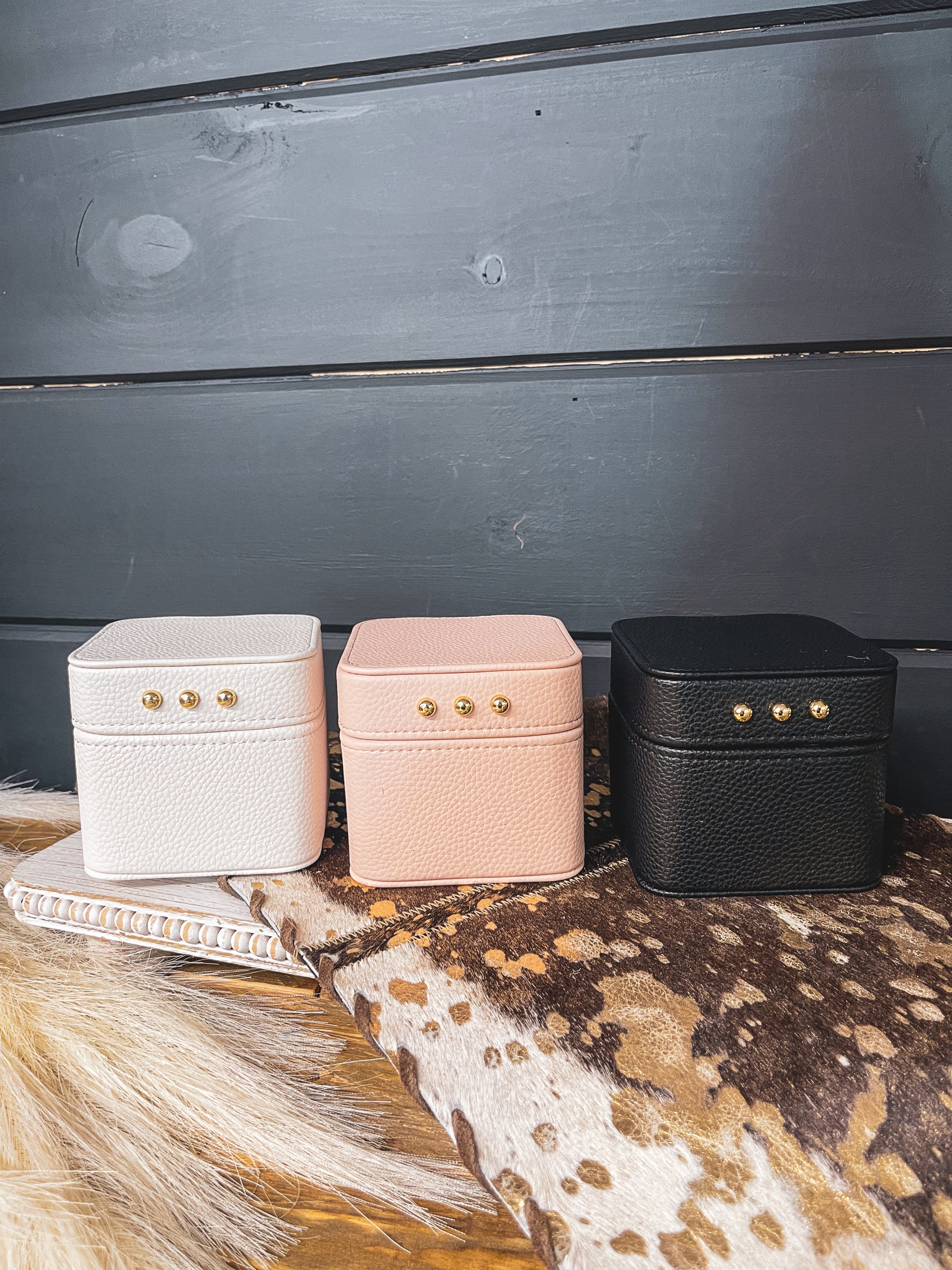 Square leather jewelry travel box with magnetic closure, individual transparent plastic zip closure bags inside and three gold balls on the front. Available in white, pink or black.