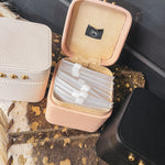 Square leather jewelry travel box with magnetic closure, individual transparent plastic zip closure bags inside and three gold balls on the front. Available in white, pink or black.