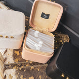 Square leather jewelry travel box with magnetic closure, individual transparent plastic zip closure bags inside and three gold balls on the front. Available in white, pink or black.
