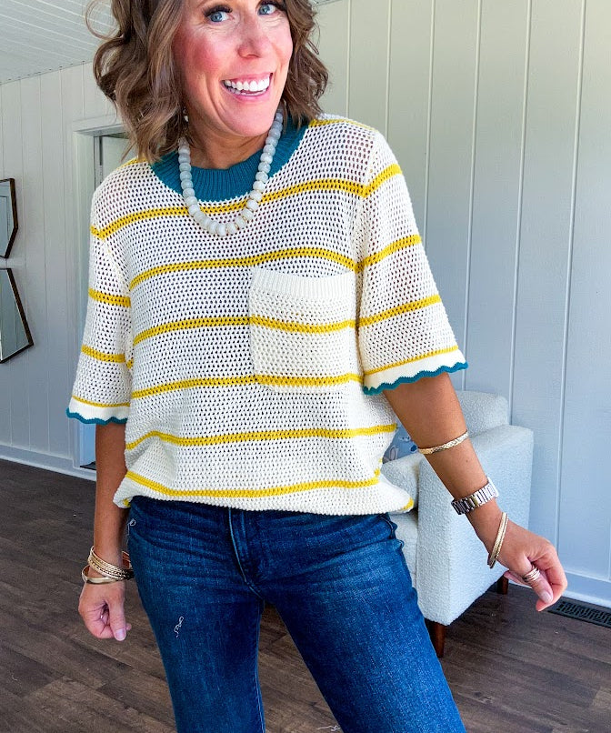 A boxy open weave cream knit that's equal parts playful and put-together. Sunshine-yellow stripes dance across the fabric while a bold teal collar and scalloped sleeve trim steal the show. The front pocket? Pure casual genius.