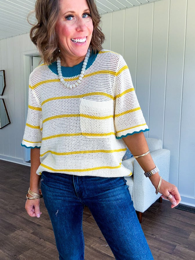 A boxy open weave cream knit that's equal parts playful and put-together. Sunshine-yellow stripes dance across the fabric while a bold teal collar and scalloped sleeve trim steal the show. The front pocket? Pure casual genius.