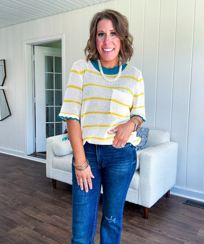 A boxy cream open weave knit that's equal parts playful and put-together. Sunshine-yellow stripes dance across the fabric while a bold teal collar and scalloped sleeve trim steal the show. The front pocket? Pure casual genius.