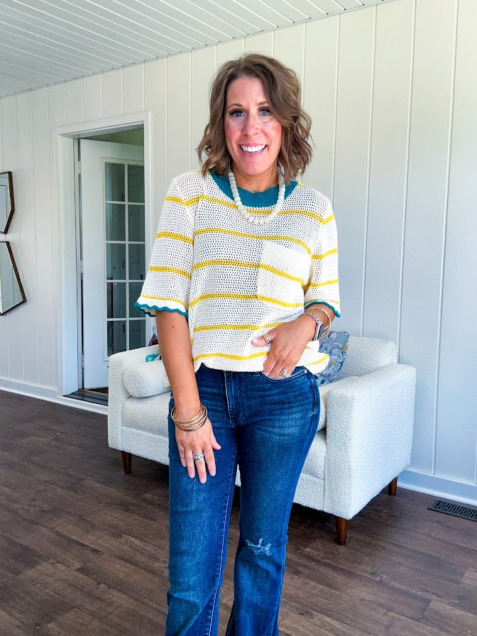A boxy cream open weave knit that's equal parts playful and put-together. Sunshine-yellow stripes dance across the fabric while a bold teal collar and scalloped sleeve trim steal the show. The front pocket? Pure casual genius.