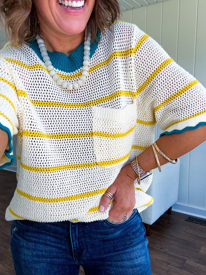 A boxy open weave cream knit that's equal parts playful and put-together. Sunshine-yellow stripes dance across the fabric while a bold teal collar and scalloped sleeve trim steal the show. The front pocket? Pure casual genius.