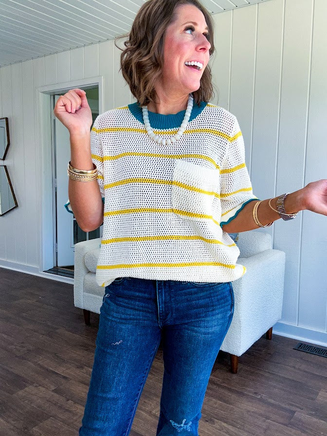 A boxy cream open weave knit that's equal parts playful and put-together. Sunshine-yellow stripes dance across the fabric while a bold teal collar and scalloped sleeve trim steal the show. The front pocket? Pure casual genius.