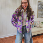 Long sleeved sherpa jacket in lavender with right ivory, green and pink florals, a detachable grey hoodie, gold zipper front and pockets.