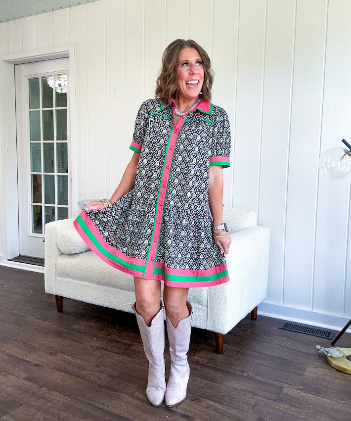 Black cotton mini dress with coral and green floral print, coral and green collar, placket, and hem with button down front and short sleeves. Has pockets.