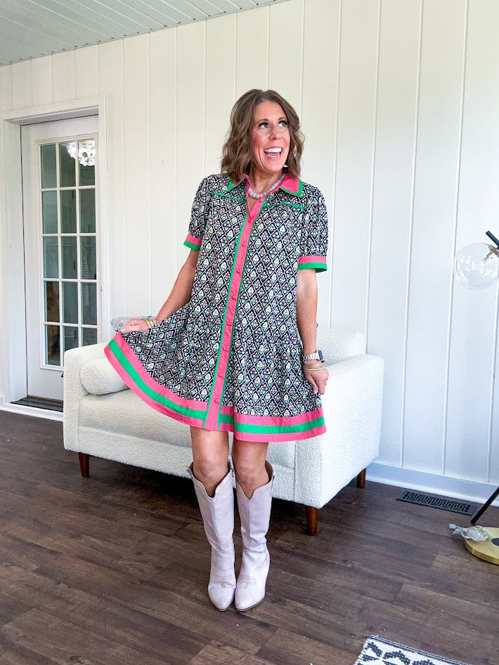 Black cotton mini dress with coral and green floral print, coral and green collar, placket, and hem with button down front and short sleeves. Has pockets.