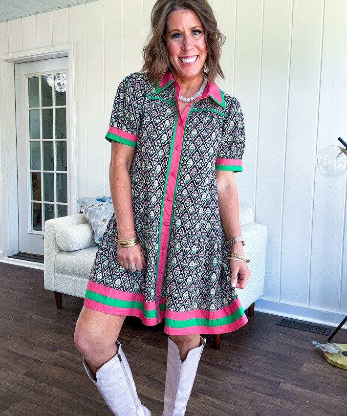 Black cotton mini dress with coral and green floral print, coral and green collar, placket, and hem with button down front and short sleeves. Has pockets.