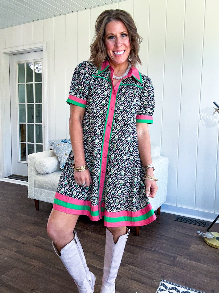 Black cotton mini dress with coral and green floral print, coral and green collar, placket, and hem with button down front and short sleeves. Has pockets.