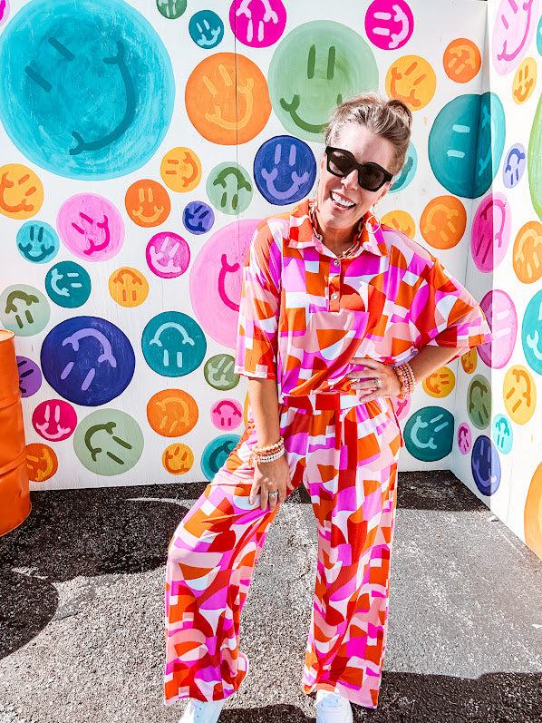 Thin, lightweight and stretchy set featuring fuchsia, orange, coral and ivory abstract print with 1/4 gold button front and collar on the short sleeved top and matching wide leg pants with elastic waist and pockets.