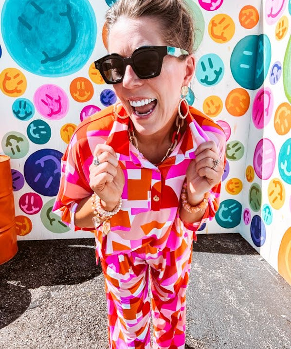 Thin, lightweight and stretchy set featuring fuchsia, orange, coral and ivory abstract print with 1/4 gold button front and collar on the short sleeved top and matching wide leg pants with elastic waist and pockets.