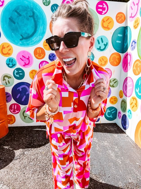 Thin, lightweight and stretchy set featuring fuchsia, orange, coral and ivory abstract print with 1/4 gold button front and collar on the short sleeved top and matching wide leg pants with elastic waist and pockets.
