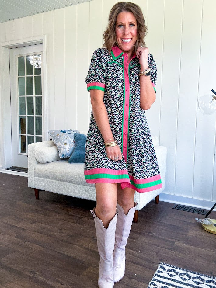 Black cotton mini dress with coral and green floral print, coral and green collar, placket, and hem with button down front and short sleeves. Has pockets.