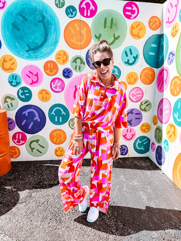 Thin, lightweight and stretchy set featuring fuchsia, orange, coral and ivory abstract print with 1/4 gold button front and collar on the short sleeved top and matching wide leg pants with elastic waist and pockets.