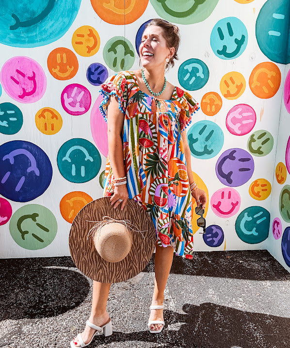 This tropical print short dress features vibrant summer hues with playful striping and fruit motifs throughout, square smocked neckline and flutter sleeves and pockets—complete with pink and blue ball tassels. Crafted from soft, lightweight fabric, it's designed to move with you all day long.