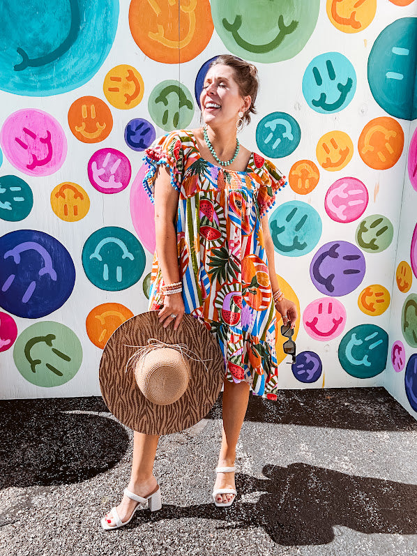 This tropical print short dress features vibrant summer hues with playful striping and fruit motifs throughout, square smocked neckline and flutter sleeves and pockets—complete with pink and blue ball tassels. Crafted from soft, lightweight fabric, it's designed to move with you all day long.
