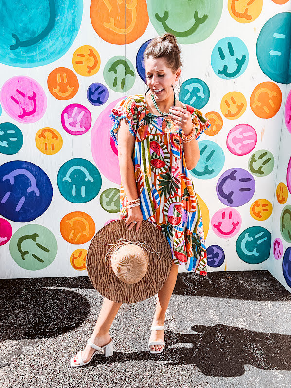 This tropical print short dress features vibrant summer hues with playful striping and fruit motifs throughout, square smocked neckline and flutter sleeves and pockets—complete with pink and blue ball tassels. Crafted from soft, lightweight fabric, it's designed to move with you all day long.
