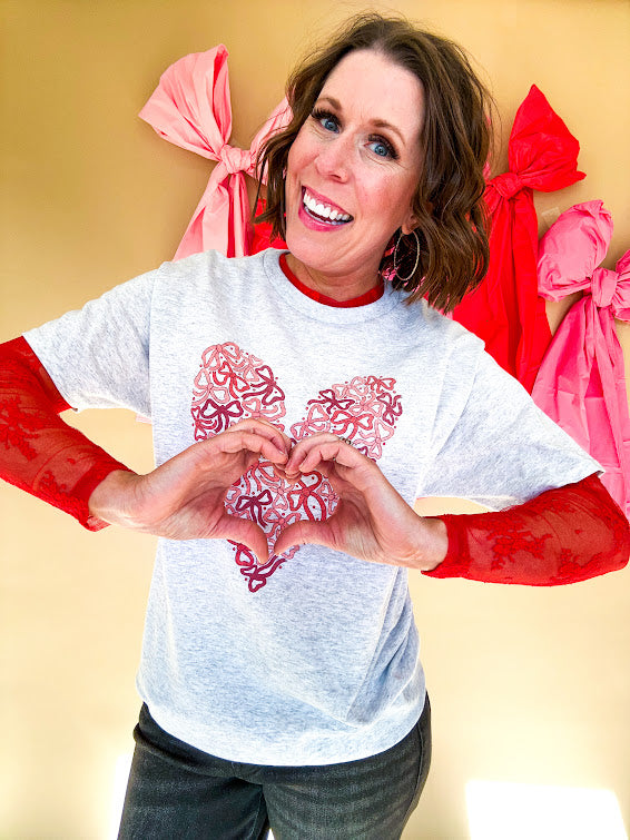 Light grey heathered tee with a pink and red heart made of bows on the front.