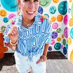 Light blue and white geometric short sleeved button down with collar and cuffed sleeves with bold orange, green and pink embroidery on the shoulders.