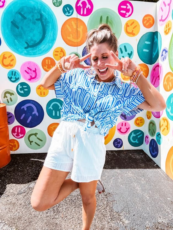 Light blue and white geometric short sleeved button down with collar and cuffed sleeves with bold orange, green and pink embroidery on the shoulders.