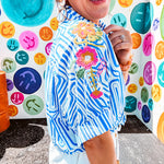 Light blue and white geometric short sleeved button down with collar and cuffed sleeves with bold orange, green and pink embroidery on the shoulders.