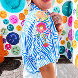 Light blue and white geometric short sleeved button down with collar and cuffed sleeves with bold orange, green and pink embroidery on the shoulders.