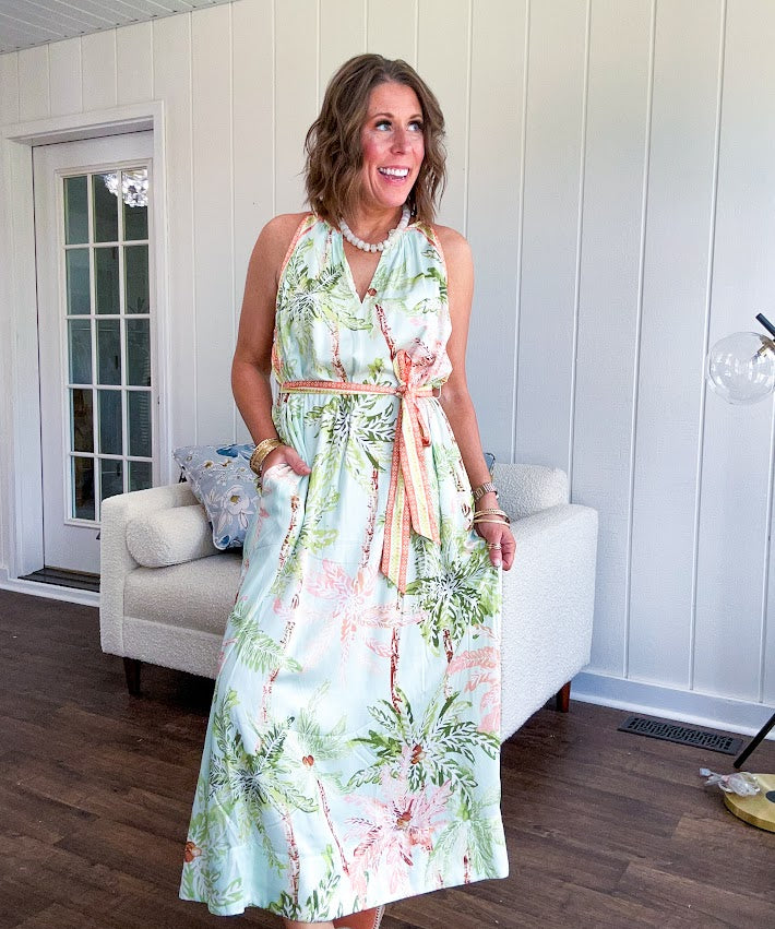 Fully lined flowy halter dress in seafoam green with green and coral tropical print, V neck with button option, matching silky belt and pockets. Midi length.