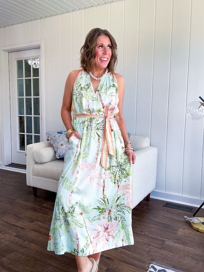 Fully lined flowy halter dress in seafoam green with green and coral tropical print, V neck with button option, matching silky belt and pockets. Midi length.