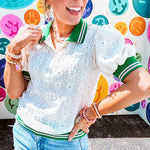 Nearly sheer ivory eyelet patterned blouse with a collar, puff sleeves and three large rhinestone floral buttons at the neckline. The collar, cuffs and hem are a contrasting bright green with pink athletic striping.