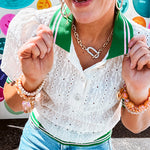 Nearly sheer ivory eyelet patterned blouse with a collar, puff sleeves and three large rhinestone floral buttons at the neckline. The collar, cuffs and hem are a contrasting bright green with pink athletic striping.