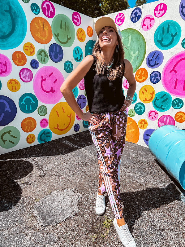 Satiny wide leg pants with drawstring waist in light brown with leopard print, light pink stars and tan stars with athletic ivory striping down the sides and side pockets.