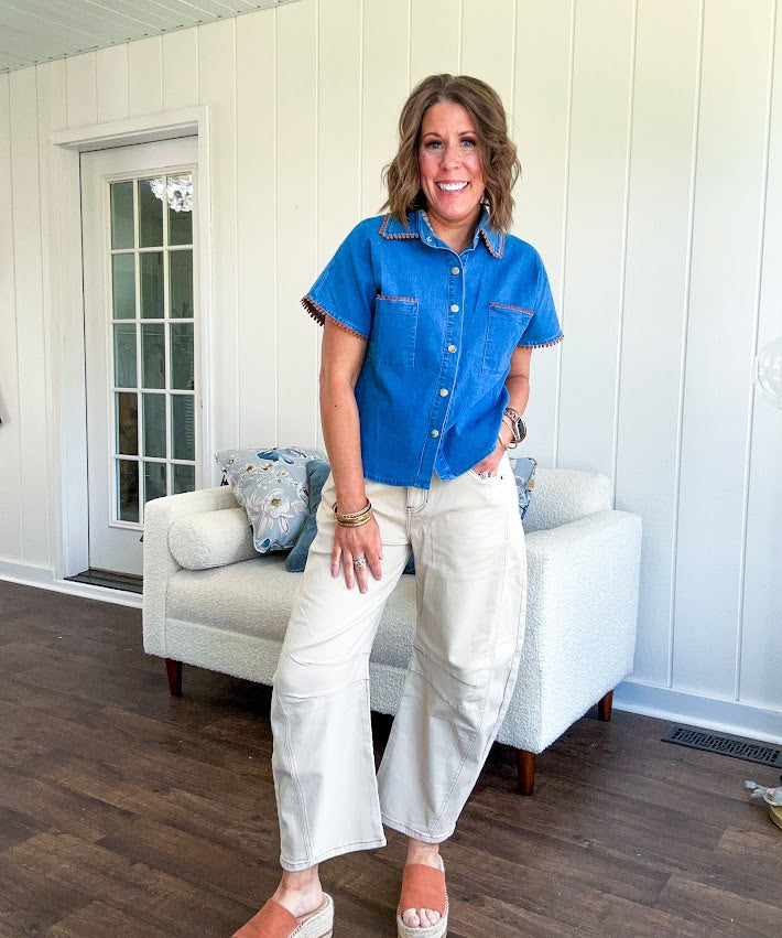 Medium denim blue short sleeved top with collar and snap button closure with two front pockets and brown trim at the collar, pockets and cuffs.