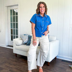 Medium denim blue short sleeved top with collar and snap button closure with two front pockets and brown trim at the collar, pockets and cuffs.