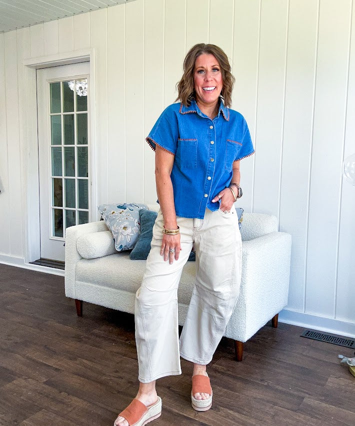 Medium denim blue short sleeved top with collar and snap button closure with two front pockets and brown trim at the collar, pockets and cuffs.