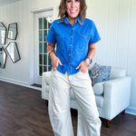 Medium denim blue short sleeved top with collar and snap button closure with two front pockets and brown trim at the collar, pockets and cuffs.