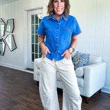 Medium denim blue short sleeved top with collar and snap button closure with two front pockets and brown trim at the collar, pockets and cuffs.