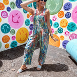 Cotton denim overalls with adjustable straps and sides with metal buttons in a paint splatter detail in cobalt blue, orange, green and yellow washed color with knee darts.