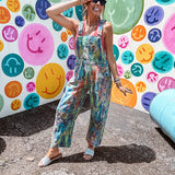Cotton denim overalls with adjustable straps and sides with metal buttons in a paint splatter detail in cobalt blue, orange, green and yellow washed color with knee darts.