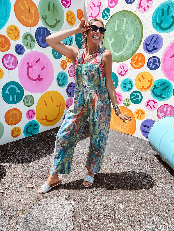 Cotton denim overalls with adjustable straps and sides with metal buttons in a paint splatter detail in cobalt blue, orange, green and yellow washed color with knee darts.