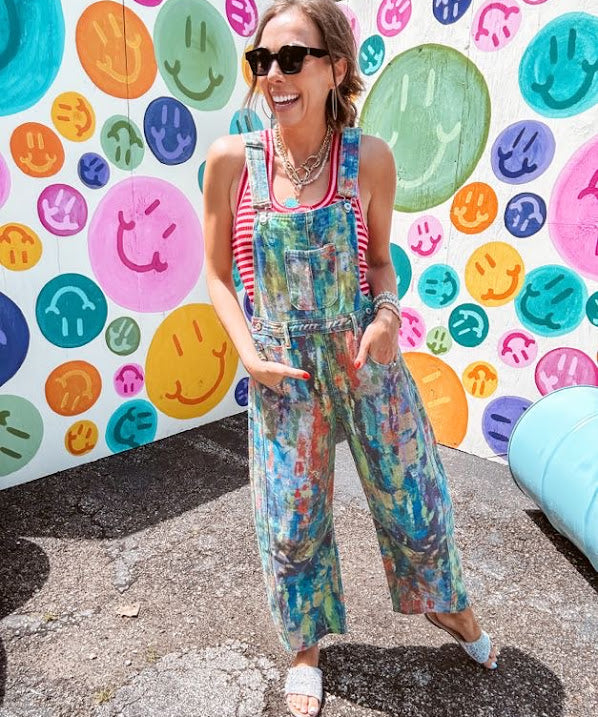 Cotton denim overalls with adjustable straps and sides with metal buttons in a paint splatter detail in cobalt blue, orange, green and yellow washed color with knee darts.