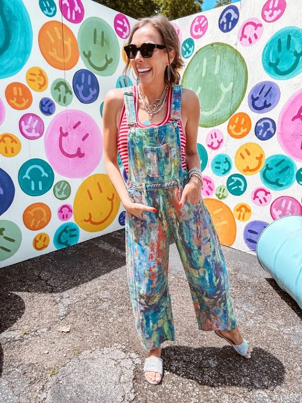 Cotton denim overalls with adjustable straps and sides with metal buttons in a paint splatter detail in cobalt blue, orange, green and yellow washed color with knee darts.