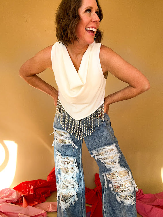 Acid washed medium denim jeans featuring heavy distressing lined with silver sequins down the legs and a wide leg, raw hem design.